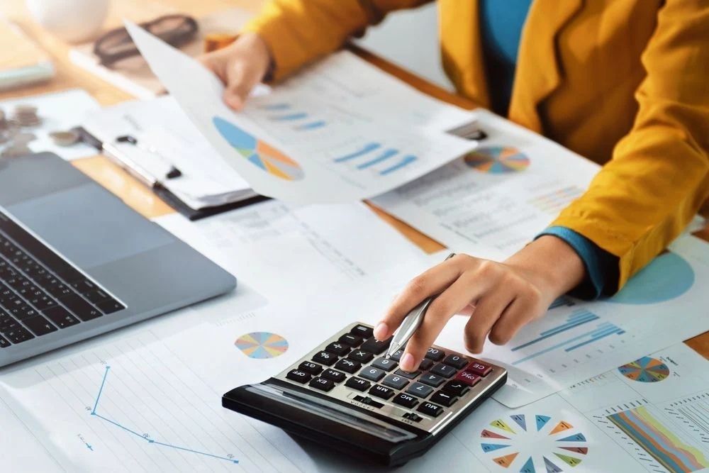 Person calculating financial figures with reports and a calculator on an office desk-